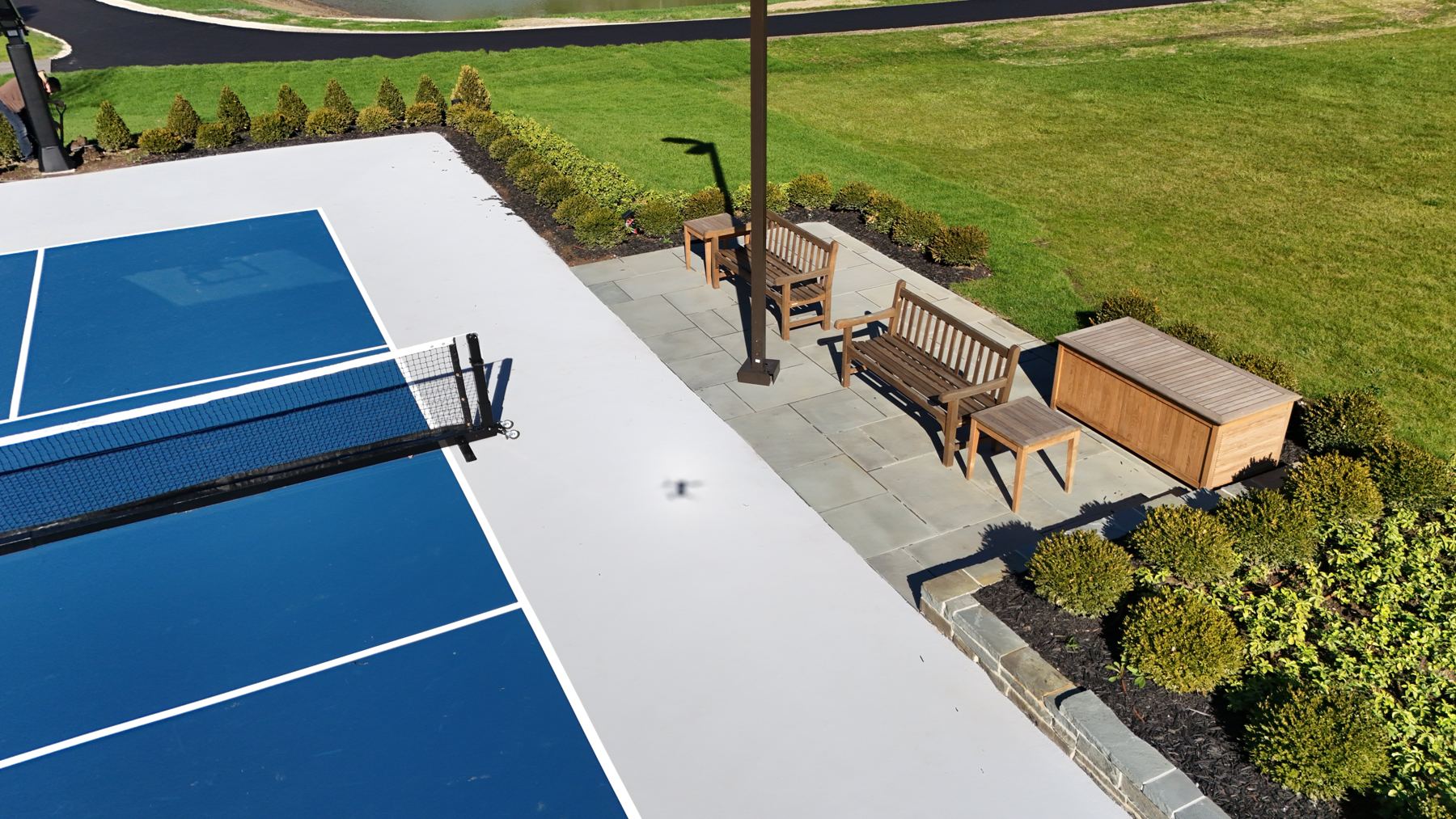 Bluestone heckler patio with teak benches, side tables and storage chest beside the court